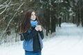 Forest winter portrait of daydreaming young lady holding cup with hot drink during snowstorm in fir forest