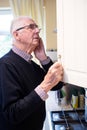 Forgetful Senior Man With Dementia Looking In Cupboard At Home Royalty Free Stock Photo