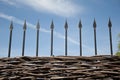 Forging a defense. Wrough iron fence on sunny blue sky. Wooden palisade with iron spikes. Beautiful decorative picket fence with Royalty Free Stock Photo