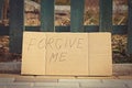 Forgiveness concept. The inscription Forgive me written by hand on cardboard against the background of a city street