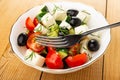 Fork in bowl of salad with cucumbers and tomato, black olives, feta cheese on wooden table Royalty Free Stock Photo