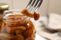 Fork with delicious marinated mushroom and glass jar on table, closeup