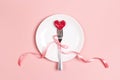 Fork with a heart on a plate on a pink table. Festive menu for Valentine`s Day. T