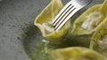 Fork impales Chinese wonton dumplings on gray plate close up. Asian traditional soup with wontons, stuffed with meat