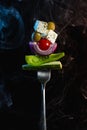 Fork with ingredients for traditional greek salad with fresh vegetables, feta cheese and olives on black background Royalty Free Stock Photo