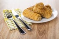 Fork and knife on napkin, fried pancake rolls with filling in white plate on wooden table