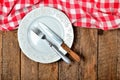 Fork and knife in empty decorative plate and red checkered tablecloth on top side on old vintage wooden table background Royalty Free Stock Photo