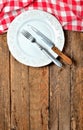 Fork and knife in empty decorative plate and red checkered tablecloth on top side on old vintage wooden table background Royalty Free Stock Photo