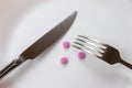 A fork, a knife and pills lie on a plate in close-up. The concept of the use of medicines Royalty Free Stock Photo