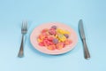 Fork, knife and pink plate with gummy candies isolated on blue Royalty Free Stock Photo