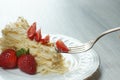 A fork with a piece of cake Napoleon on a plate, decorated with a red ripe strawberry on a table