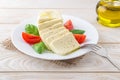 Fork on a plate with rectangular slices of mozzarella cheese, fresh basil and quarters of tomato over a wooden table. Healhy