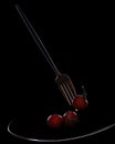 Fork with small tomatoes on a black background, on a plate Royalty Free Stock Photo