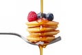 A fork with a stack of mini pancakes drizzled with syrup and topped with berries creates a delicious breakfast close-up. Royalty Free Stock Photo