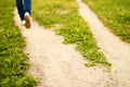 Forked footpath among green grass and foot of person going away