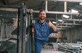 In the forklift, showing thumb up. Factory worker in blue uniform is indoors