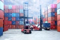 Forklift truck lifting cargo container in shipping yard or dock yard against sunrise sky with cargo container stack in background