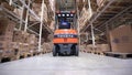 Forklift Trucks Move Between Large Metal Shelves at a Modern Warehouse and Unload Pallets with Cardboard Boxes