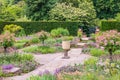 Formal flagged secluded garden with standard roses and vintage vase.