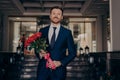 Formally dressed attractive businessman waiting for girlfriend with bouquet of roses