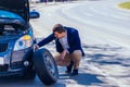 A formally dressed gentleman wearing a blue blazer is changing the flat tire on his car while being parked next to a busy