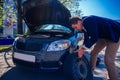 A formally dressed gentleman wearing a blue blazer is changing the flat tire on his car while being parked next to a busy