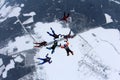 Formation skydiving. A group of skydivers is above snowy ground.