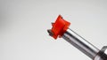 Forstner bit with a red metal cutter rotating in an electric drill on a white background.