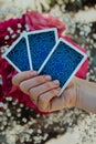 Fortune teller holding oracle cards in hand on flowers background. Tarot reader. Future prediction, esoteric, intuition Royalty Free Stock Photo
