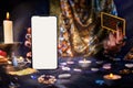 The fortune teller is holding a Tarot card and a smartphone with a white screen. Magic aura. Mock up. Close-up. The concept of