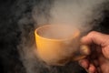 Fortune-telling on coffee. Close-up sorcerer hand holding a yellow mug with steam on a dark background Royalty Free Stock Photo