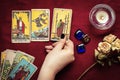 Fortunetellers hand with black manicure lays out tarot cards, crystal, candle, dry roses on red tablecloth Flat lay Top view