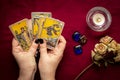 Fortuneteller`s hand with black manicure lays out tarot cards, crystal, candle, dry roses on red tablecloth