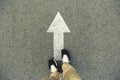Forward arrow painted on an asphalt road. Top view of the legs a