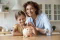 Happy smiling mom cuddling small girl putting coin to piggybank. Royalty Free Stock Photo