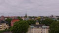 Forwards fly above green trees in city park. Revealing old residential houses in urban borough. Tall church tower in