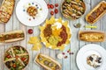 Top view photo of Mexican dishes, hot dogs, salads in home service bowl and poles with lacasitos on wooden background