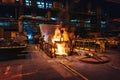 Foundry workshop interior, molten iron pouring from blast furnace into ladle container and workers founders control