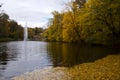 Fountain in autumn nature with trees and lake with yellow fallen leaves in water Royalty Free Stock Photo