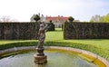 A fountain in the form of a statue stands in a pond in the foreground. An English country house is in the background