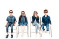 Four amazed kids in 3d glasses sitting on chairs on white.