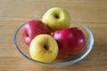 Four apples, two yellow and two red, in a glass bowl on a wooden table