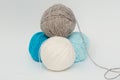 Four balls of yarn for knitting lie in the form of a pyramid on a white background. Gray, white, blue, blue tangle. The concept is