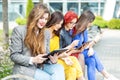 Four beautiful girls with gadgets are sitting on the bench. The concept of the Internet, social networks, study and lifestyle Royalty Free Stock Photo