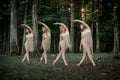 Four beautiful slender young female dancers dance synchronously in the forest.