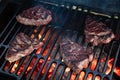 Four beef steaks being grilled over hot coals