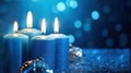 Four blue Advent candles within lush evergreen branches. Christmas time, Advent season. Flickering flames cast soft, inviting glow