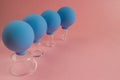 Four blue cosmetic vacuum jars of different sizes made of glass and rubber on pink background.