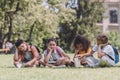 Bored multicultural schoolchildren with books sitting on lawn in park