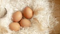 Four brown hen eggs and chicken feather on white paper in wooden basket, top view photo Royalty Free Stock Photo